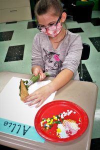 student in mask and glasses decorating with icing