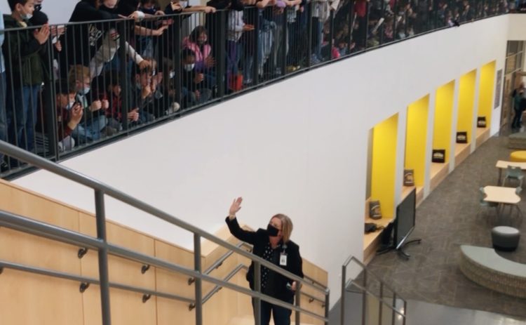woman in mask on school stairs waving to students above