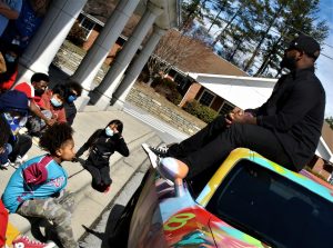 children on ground looking up at man on top of car 