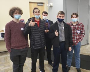 5 people inside smiling behind masks, holding plaque