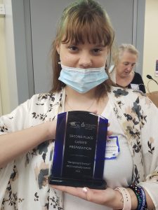 student in mask holding plaque