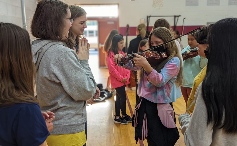 elementary student trying out violin while 3 others watch