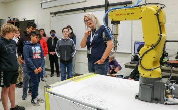 group of students in engineering classroom, teacher pointing to machine