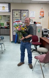 man holding balloon and flowers in classroom