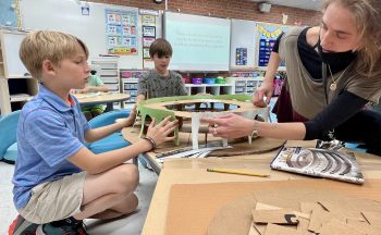 student and teacher working on model Colosseum in foreground, student in background