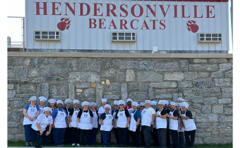 Photo of culinary students in front of Hendersonville High School sign.