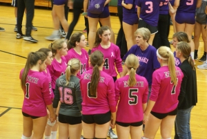 Coach Moon on the gym floor with at least 10 volleyball players in a circle.