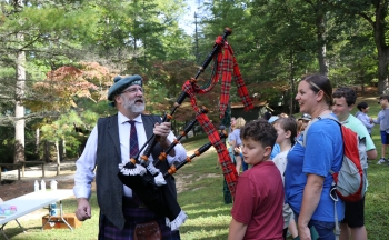 Man in traditional Scottish attire and carrying a bagpipe speaks with students.