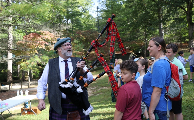 Man in traditional Scottish attire and carrying a bagpipe speaks with students.