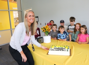 Ms. Schneider posing with her cake with a few students from her class standing behind her. 
