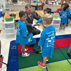 Superintendent Mark R. Garrett helping three kindergarteners put on their new t-shirts. 