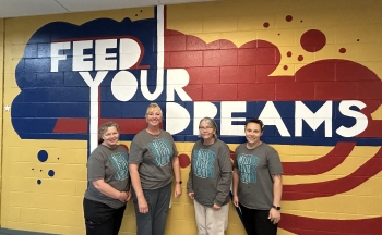 A group photo of Ms. Kristine, Ms. Staci, Ms. Rita, and Ms. Chantel in front of a wall that says "feed your dreams."