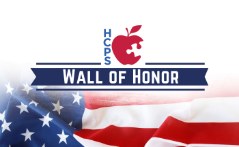 An image of text that says "Wall of Honor." There is a background image of an american fla. There is also the red "HCPS" apple.