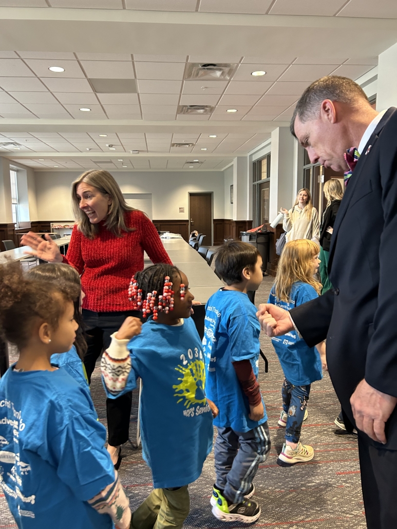 The superintendent giving a fist bump to a kindergartener. There are about three other kindergarteners in the photo. 