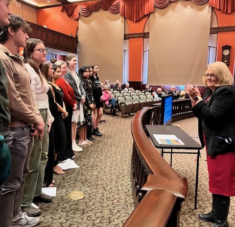 About 10 students standing before the county comissioners with the chairman Rebecca MccCall introducing them.