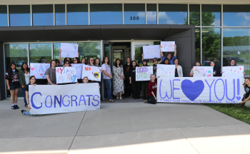 Over 20 students hold signs outside of the building and Marley is in the center of the photo.