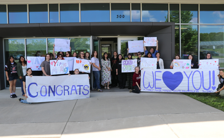 Over 20 students hold signs outside of the building and Marley is in the center of the photo.