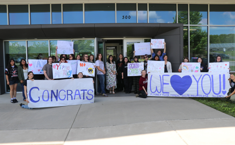 Over 20 students hold signs outside of the building and Marley is in the center of the photo.