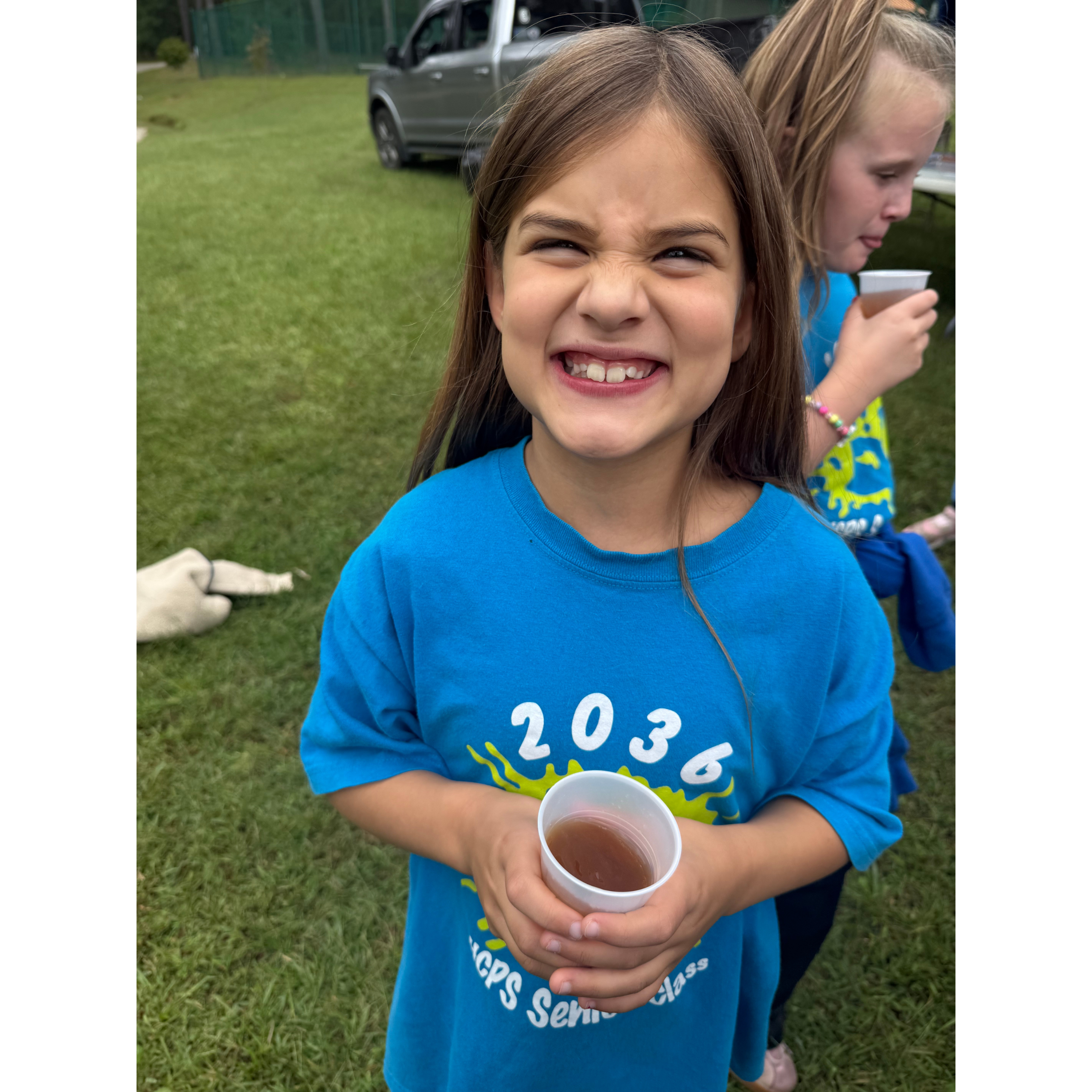 A girl smiling big and holding a cup of apple cider. 