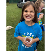 A girl smiling big and holding a cup of apple cider.