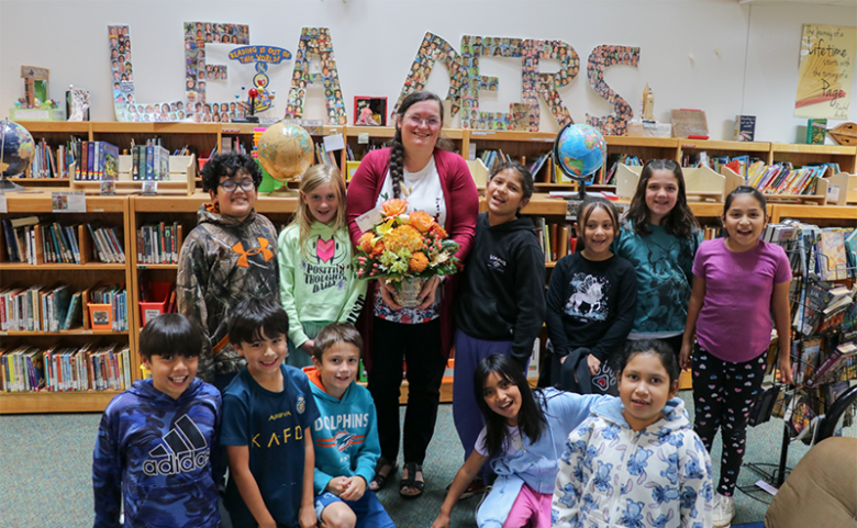 Debra Ramsey poses with a class in the library. She is holding a beautiful vase of flowers.