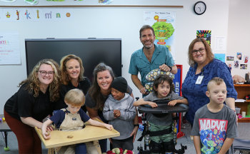 Erin Celej poses with four students, three staff members and Etowah Principal, Dr. Amanda Childers. They are in a classroom.