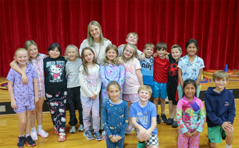 Ms. Schwartz poses for a photo with her third grade class. There are 16 students.