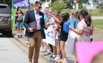 Cody Merriman walking through a parade of students outside the school. The students have signs and balloons.